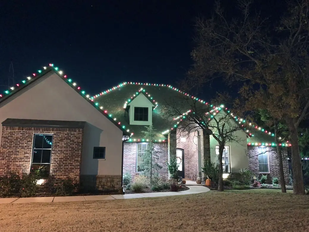 A single-storey brick home at night with red, green and warm white bulbs following every gable and roofline.